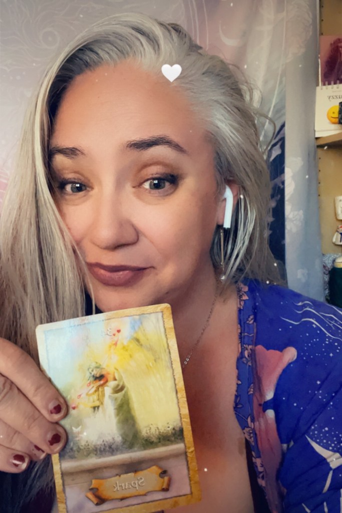 Photo of Janet wearing a grey sweater and holding the Hierophant tarot card right below her face.