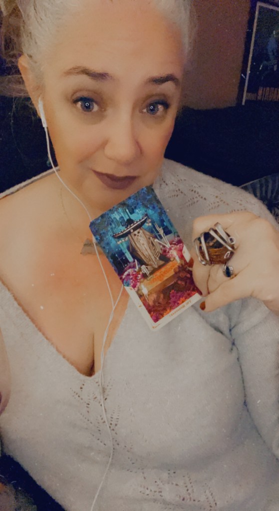 Photo of Janet wearing a grey sweater and holding the Hierophant tarot card right below her face.